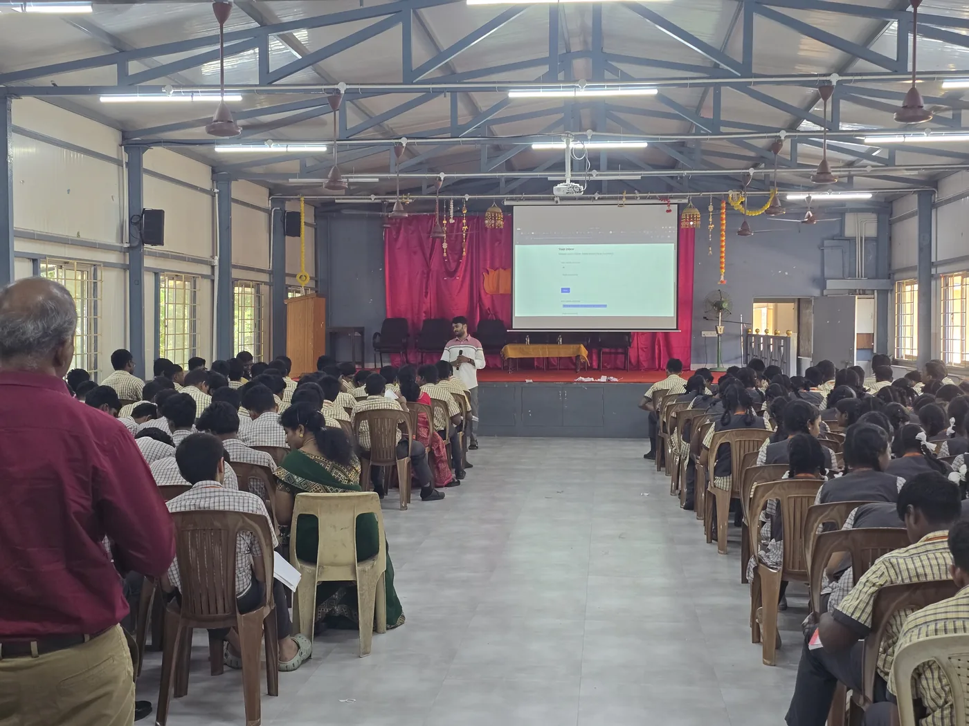 An OxygenLabs instructor presenting an AI workshop to school students, with a live tool demo on the projector screen behind him.